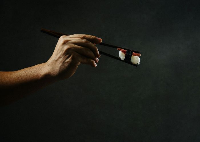 A hand holding a wagyu beef nigiri sushi out with chopsticks, set against a black background.